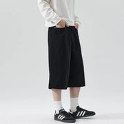 Person wearing black wide-leg pants, white shirt, and black sneakers on a light gray background