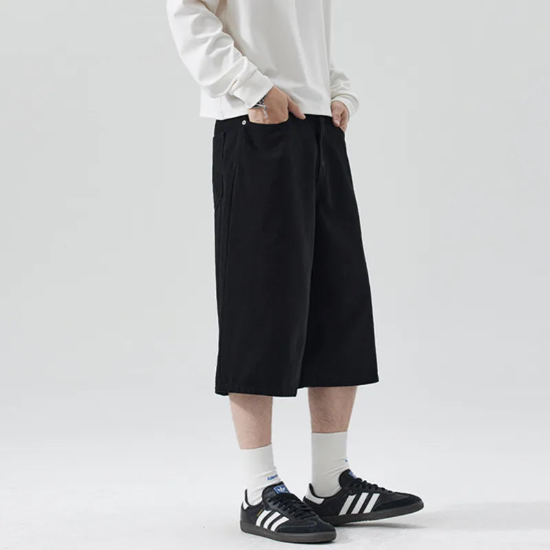 Person wearing black wide-leg pants, white shirt, and black sneakers on a light gray background