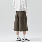 Person wearing brown wide-leg pants, white sweatshirt, and Adidas shoes on a plain background