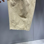 A close-up of a light beige or khaki fabric garment, showing the texture and hem stitching, held against a gray background.