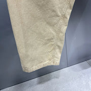 Close-up of a light beige or khaki fabric garment, showing the texture and hem detail against a dark gray background.