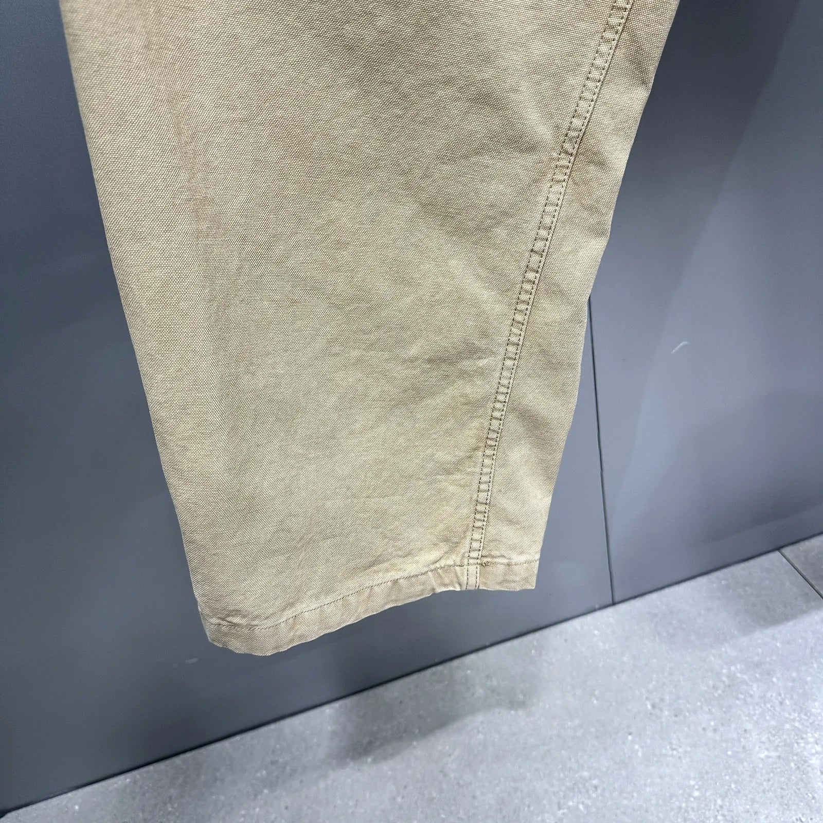 Close-up of a light beige or khaki fabric garment, showing the texture and hem detail against a dark gray background.