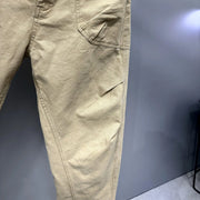 Close-up of tan cargo pants showing the side pocket and leg construction against a dark gray background.