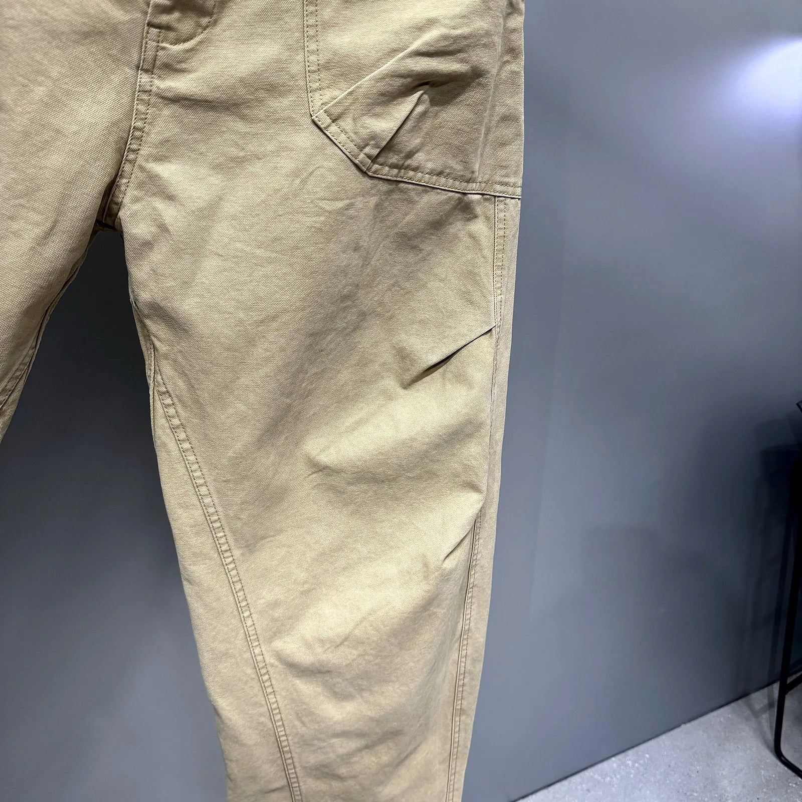 Close-up of tan cargo pants showing the side pocket and leg construction against a dark gray background.