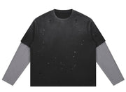 A long-sleeve distressed crewneck shirt with a black body and faded gray sleeves, featuring small white speckled details across the front, shown on a plain white background.