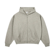 A light oat gray zip-up hoodie with a front kangaroo pocket, displayed flat against a textured off-white background with text overlays.