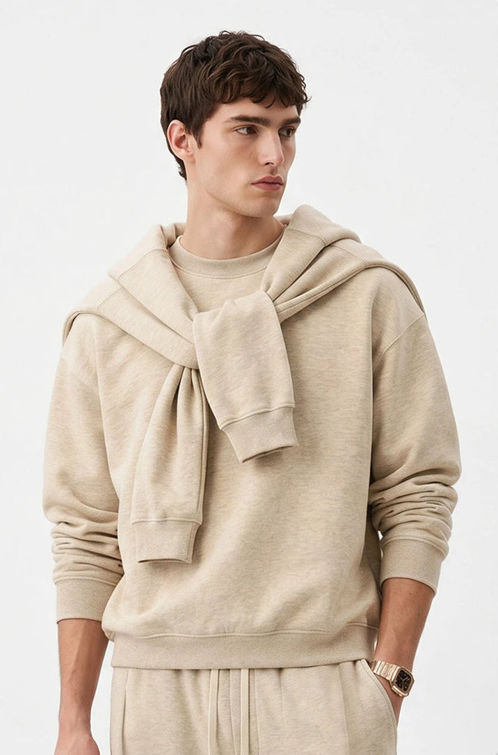 A male model wearing a beige hooded sweatshirt with a large knotted bow detail at the neck, paired with matching beige sweatpants, set against a clean white background.