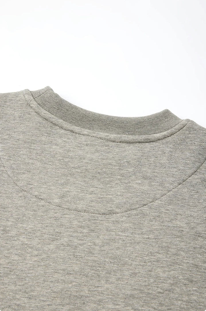 Close-up detail shot of a light gray heather crewneck sweatshirt, showing the curved reinforced back panel and collar stitching, with Chinese and English text at the bottom describing the feature.
