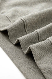 Close-up of a gray ribbed knit garment corner showing the cuff construction and fabric texture, with Chinese text below describing the reinforced hem detail.