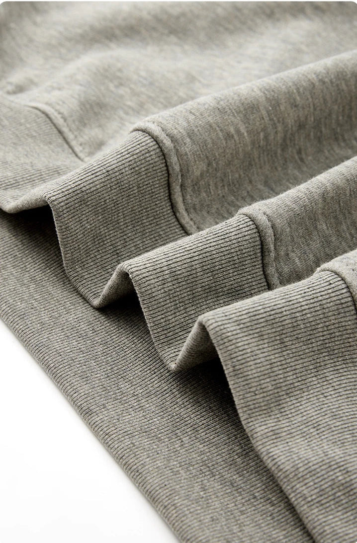 Close-up of a gray ribbed knit garment corner showing the cuff construction and fabric texture, with Chinese text below describing the reinforced hem detail.