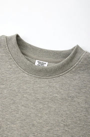 Close-up of a light gray heather crewneck sweatshirt showing the ribbed collar and inner neck label, with Chinese and English text at the bottom describing the collar features.