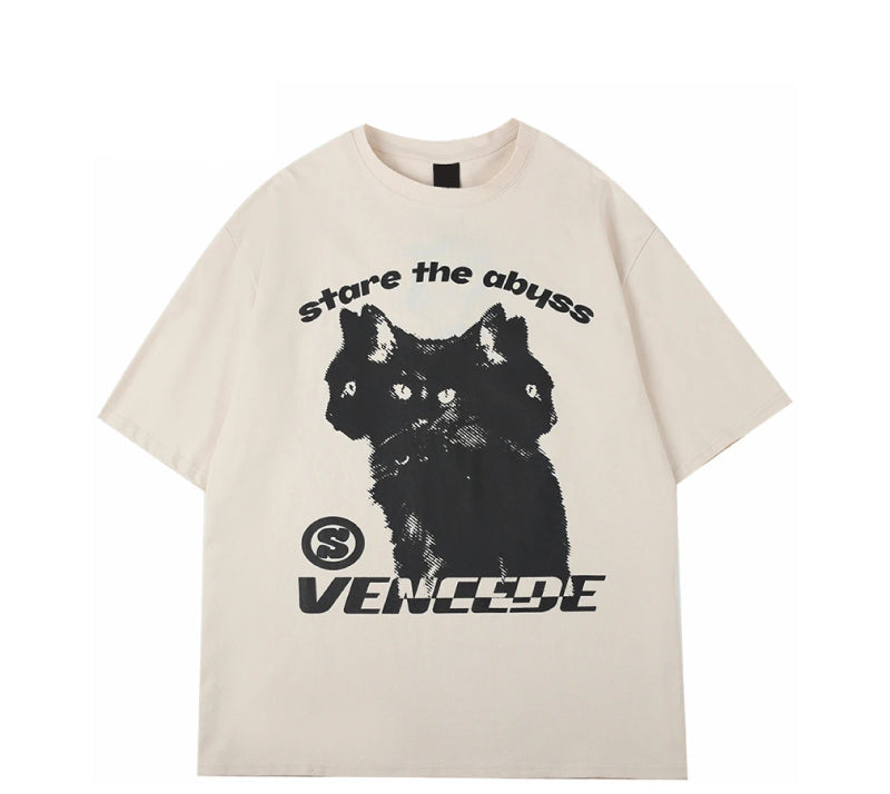 An off-white short-sleeve t-shirt with a black graphic of a three-headed cat, the text 'stare the abyss' above it, and 'VENCEDE' below it, displayed on a clean white background.